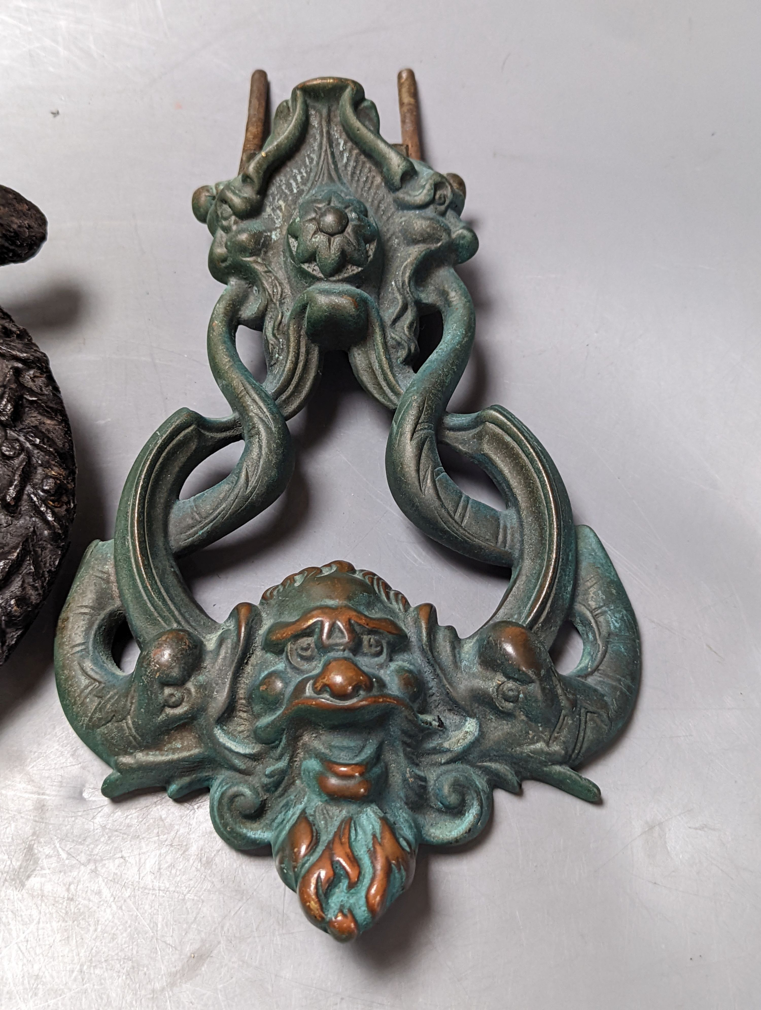 A grotesque bronze door knocker, 23 cm high and a similar cast-iron example